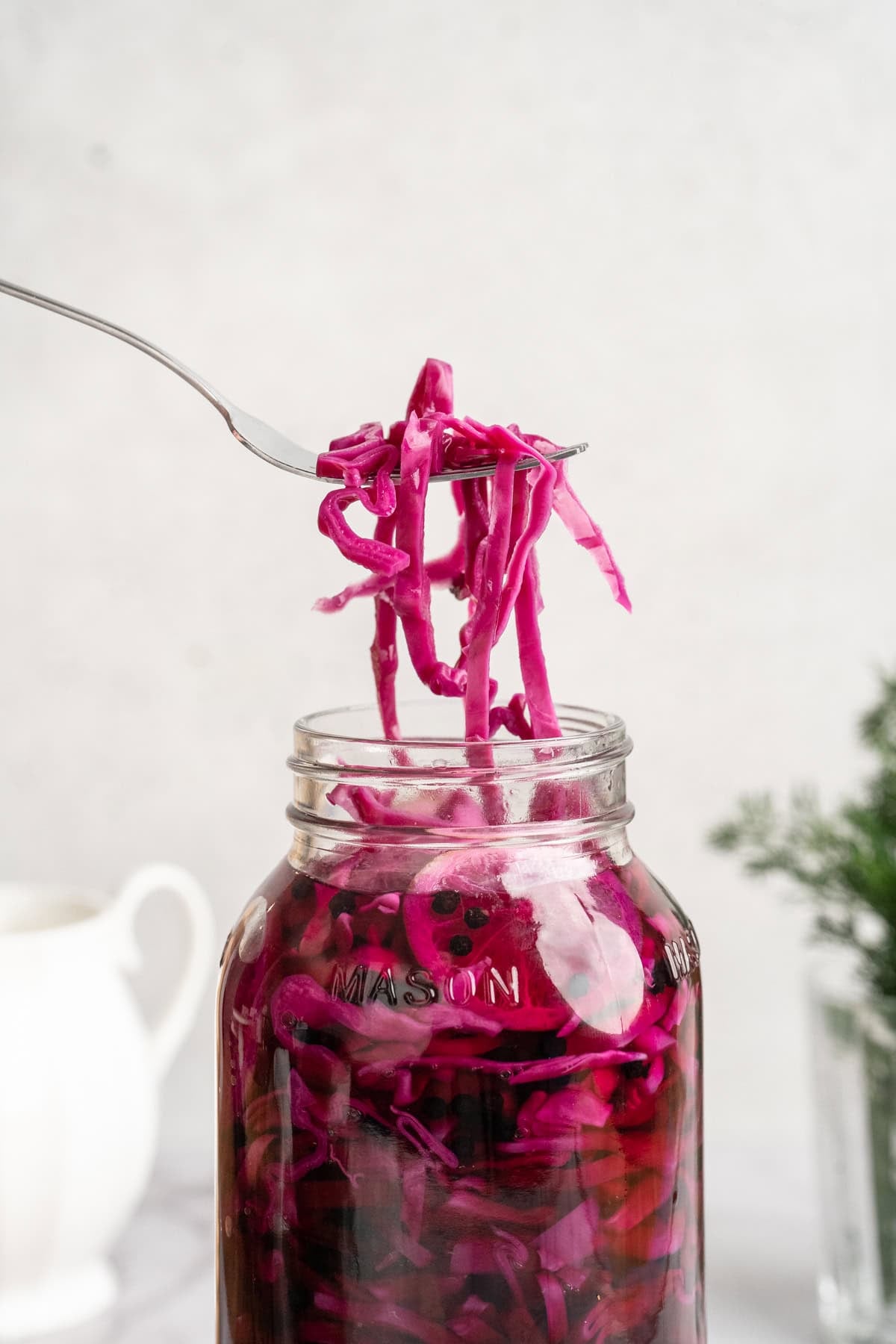 This quick pickled cabbage comes out incredibly flavourful (brine-y, tangy, and a tad sweet) with a subtle crunch. And in just a few minutes! A fork lifting some quick pickled red cabbage from a jar.