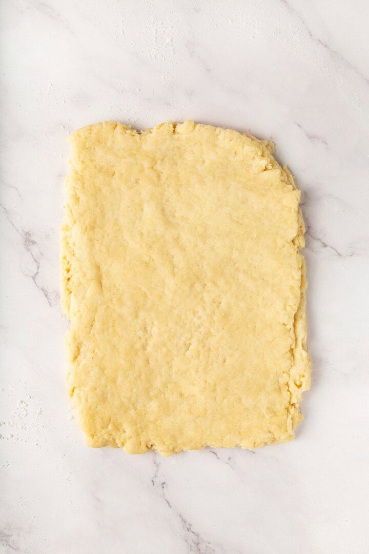 Strawberry shortcake recipe sandwiches sweet, syrupy macerated strawberries and fluffy vegan whipped cream between flaky homemade biscuits. Vegan biscuit dough shaped into a rectangle after folding.