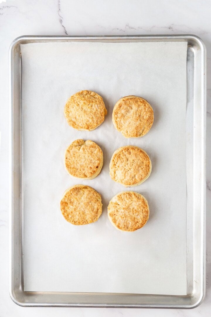 Strawberry shortcake recipe sandwiches sweet, syrupy macerated strawberries and fluffy vegan whipped cream between flaky homemade biscuits. Vegan biscuits cooling on a baking sheet.