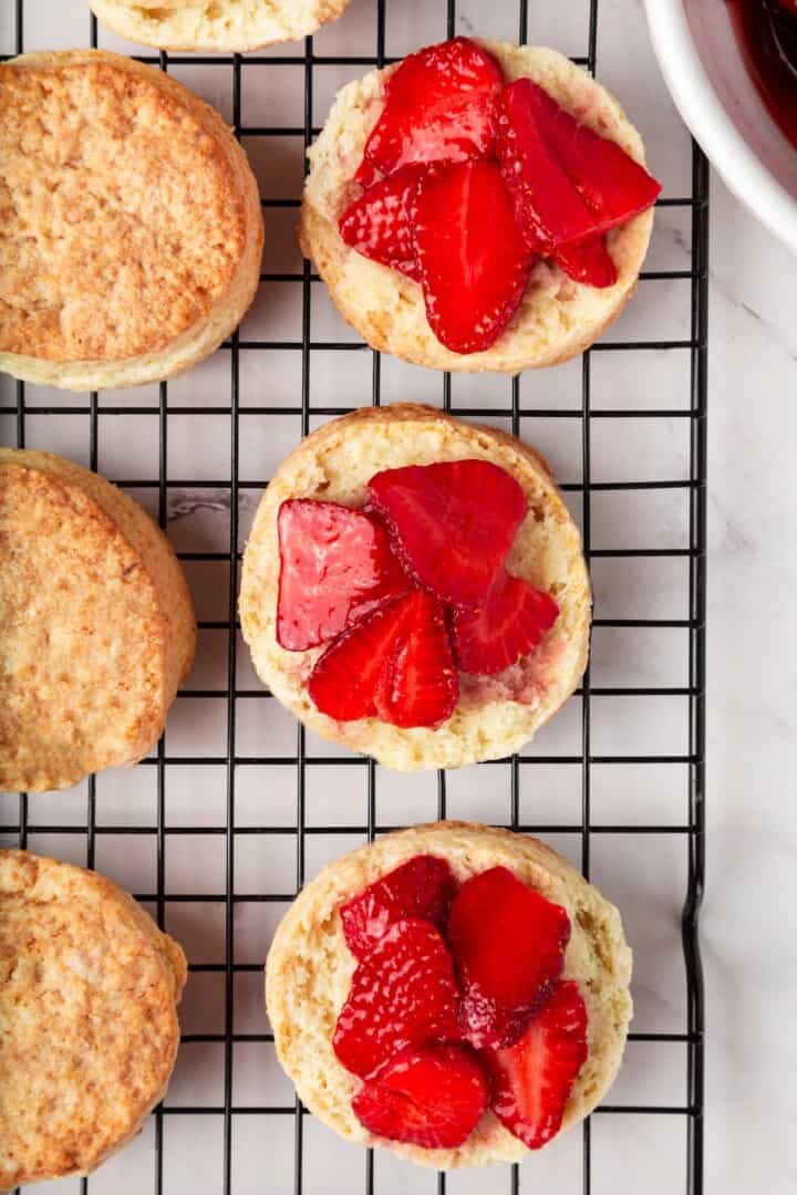 Strawberry shortcake recipe sandwiches sweet, syrupy macerated strawberries and fluffy vegan whipped cream between flaky homemade biscuits. Layering macerated strawberries onto halved vegan biscuits.