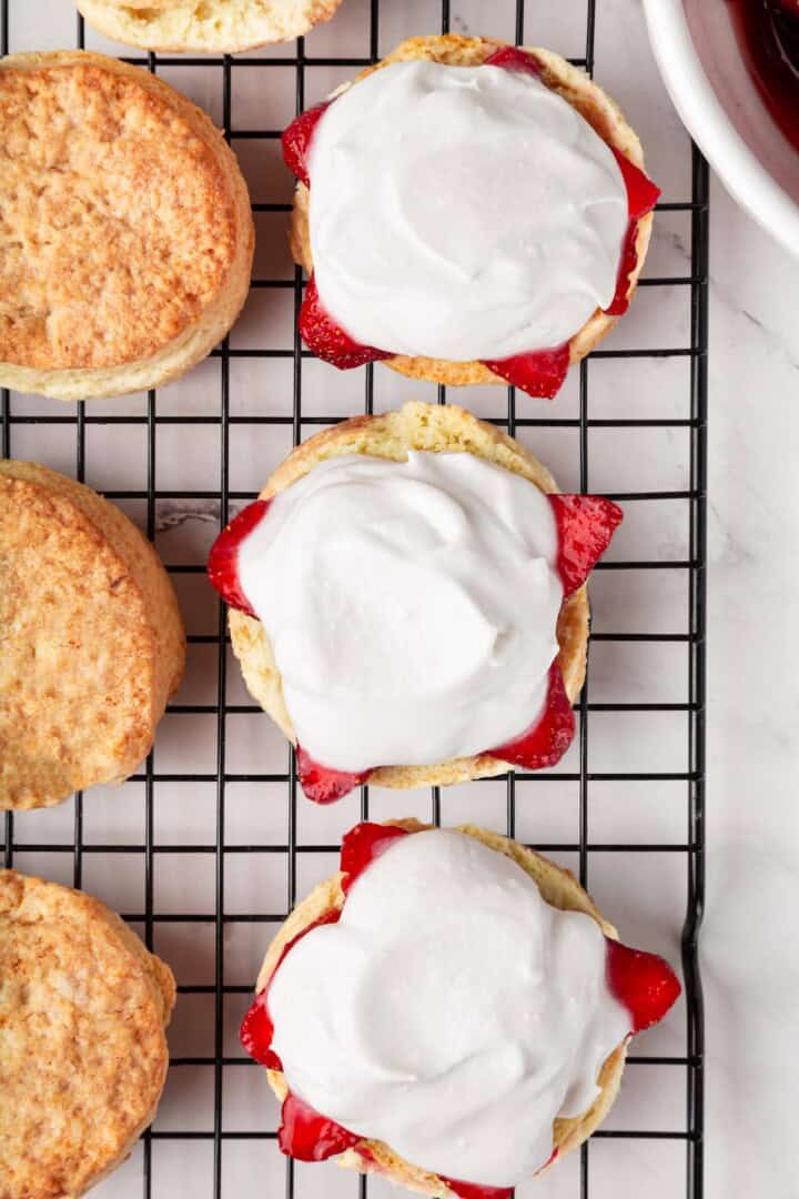 Strawberry shortcake recipe sandwiches sweet, syrupy macerated strawberries and fluffy vegan whipped cream between flaky homemade biscuits. Layering vegan whipped cream over macerated strawberries in halved vegan biscuits.