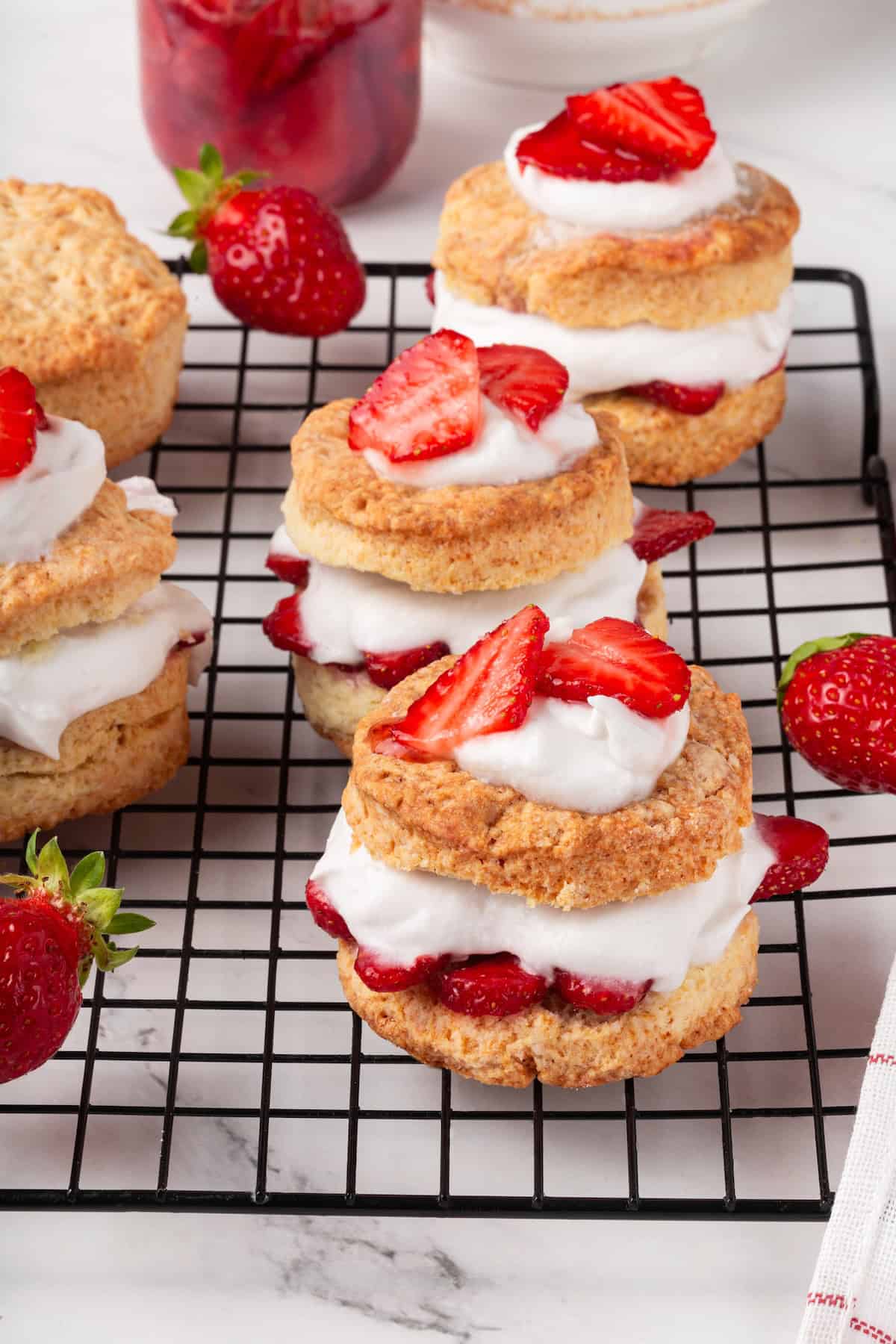 Strawberry shortcake recipe sandwiches sweet, syrupy macerated strawberries and fluffy vegan whipped cream between flaky homemade biscuits. Vegan strawberry shortcakes arranged on a wire rack with a few fresh berries.
