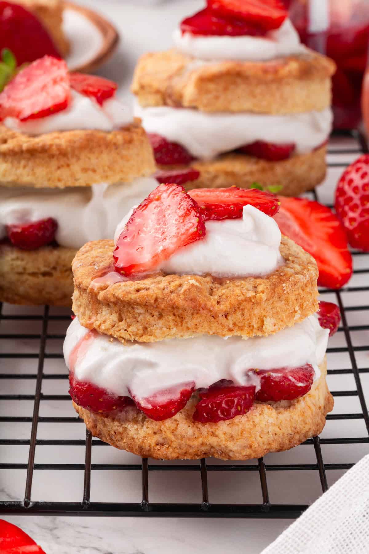Strawberry shortcake recipe sandwiches sweet, syrupy macerated strawberries and fluffy vegan whipped cream between flaky homemade biscuits. Side-view of a vegan strawberry shortcake on a cooling rack.