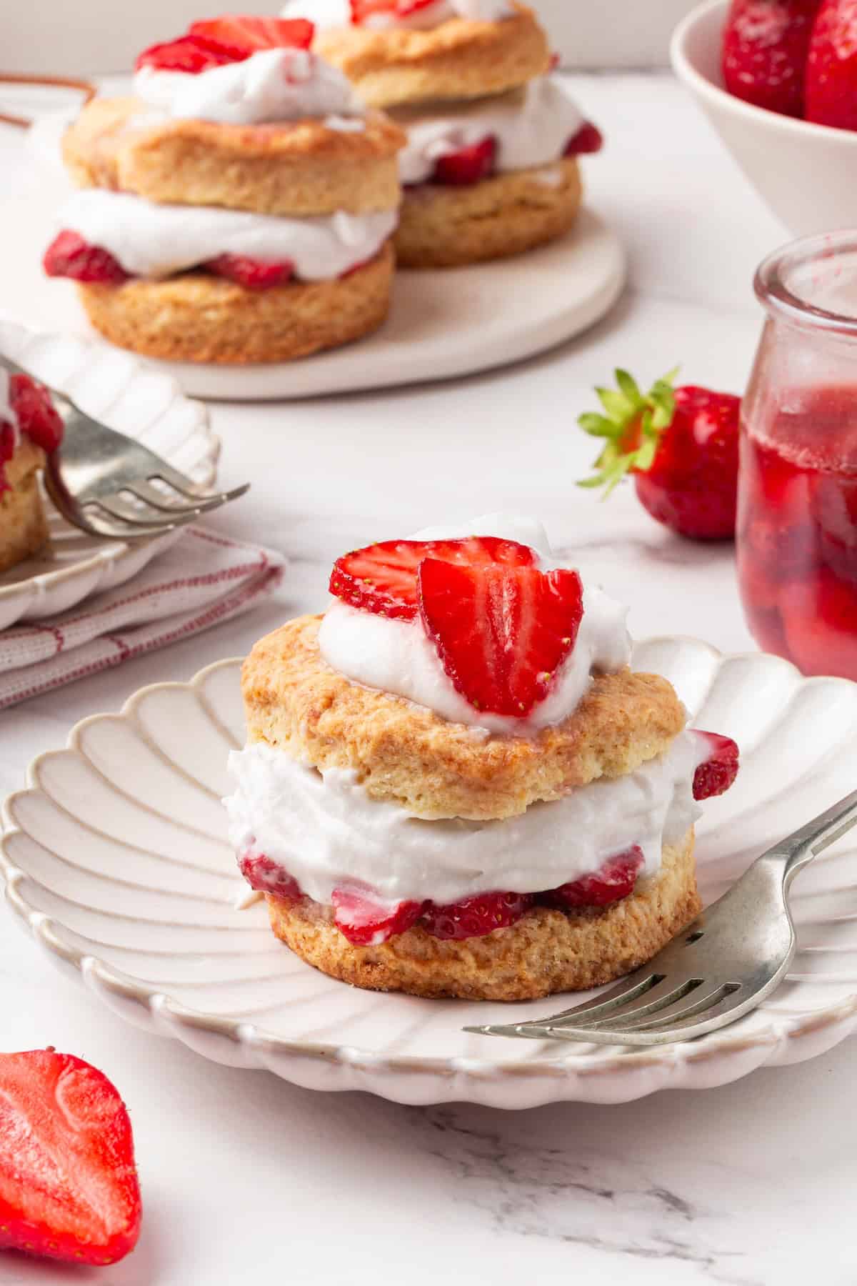 Strawberry shortcake recipe sandwiches sweet, syrupy macerated strawberries and fluffy vegan whipped cream between flaky homemade biscuits. Strawberry shortcake served on a white plate.