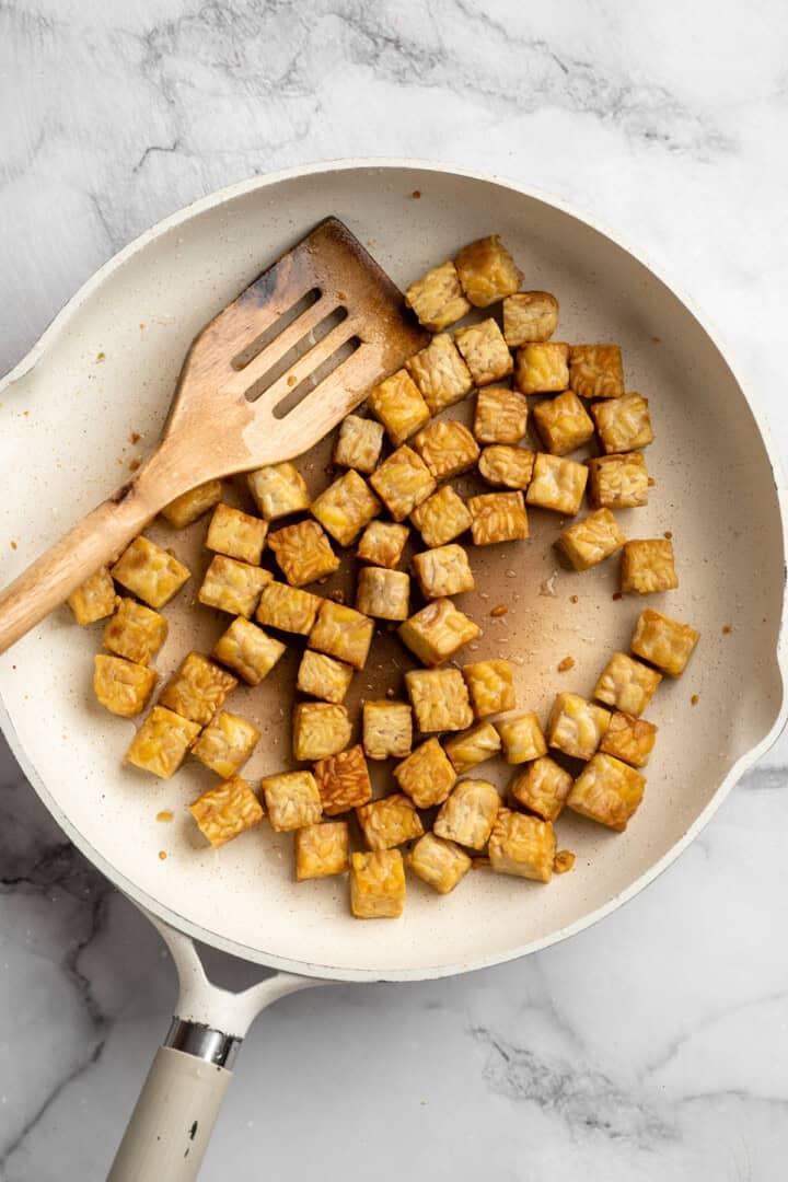 This 35-minute tempeh stir fry combines crispy golden tempeh, tender veggies, and a creamy, savoury-sweet Thai-style peanut sauce. Crisping up some cubed tempeh in a pan.