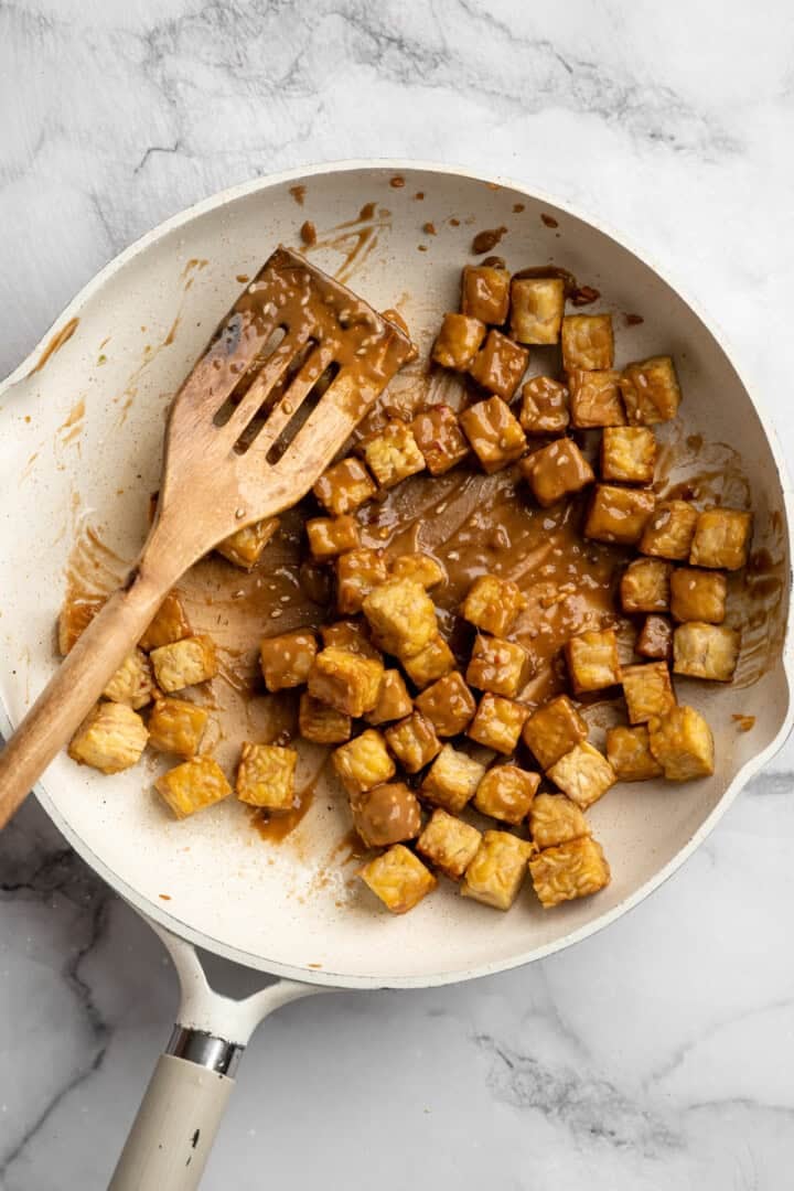 This 35-minute tempeh stir fry combines crispy golden tempeh, tender veggies, and a creamy, savoury-sweet Thai-style peanut sauce. Adding a couple of tablespoons of peanut sauce to crispy tempeh in a pan.