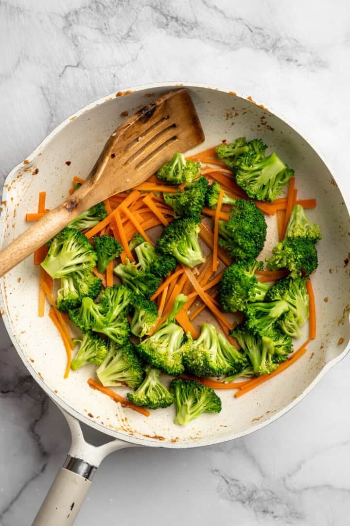 This 35-minute tempeh stir fry combines crispy golden tempeh, tender veggies, and a creamy, savoury-sweet Thai-style peanut sauce. Stir frying broccoli and carrots in a pan.