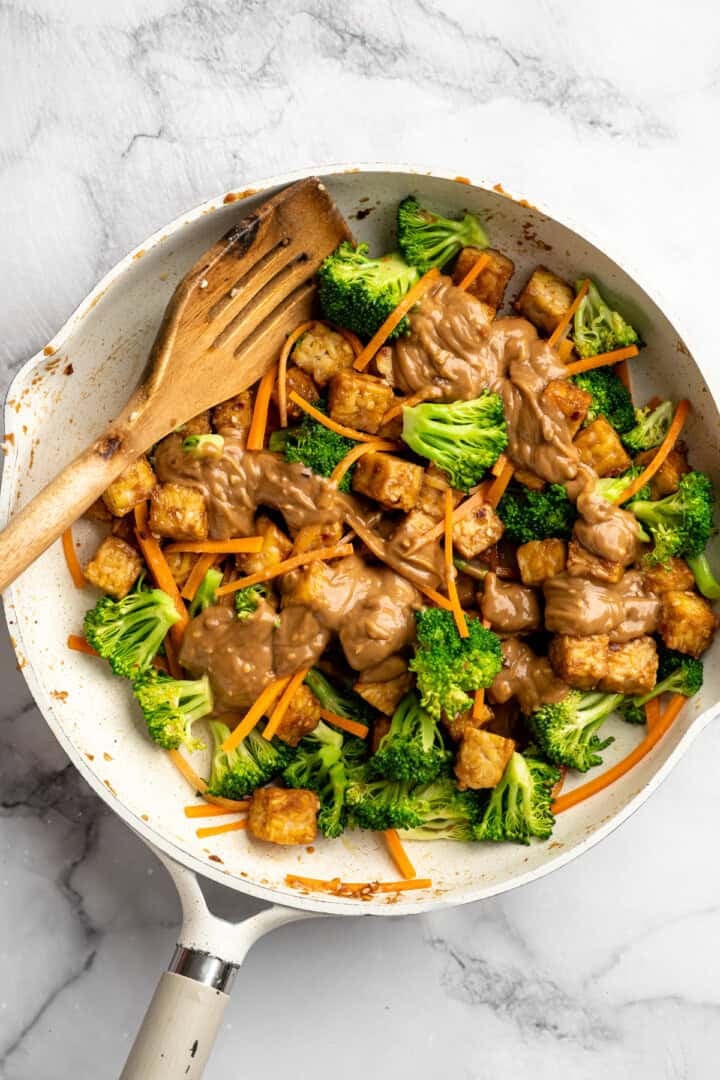 This 35-minute tempeh stir fry combines crispy golden tempeh, tender veggies, and a creamy, savoury-sweet Thai-style peanut sauce. Adding crispy tempeh and peanut sauce to a pan with stir fried veggies.