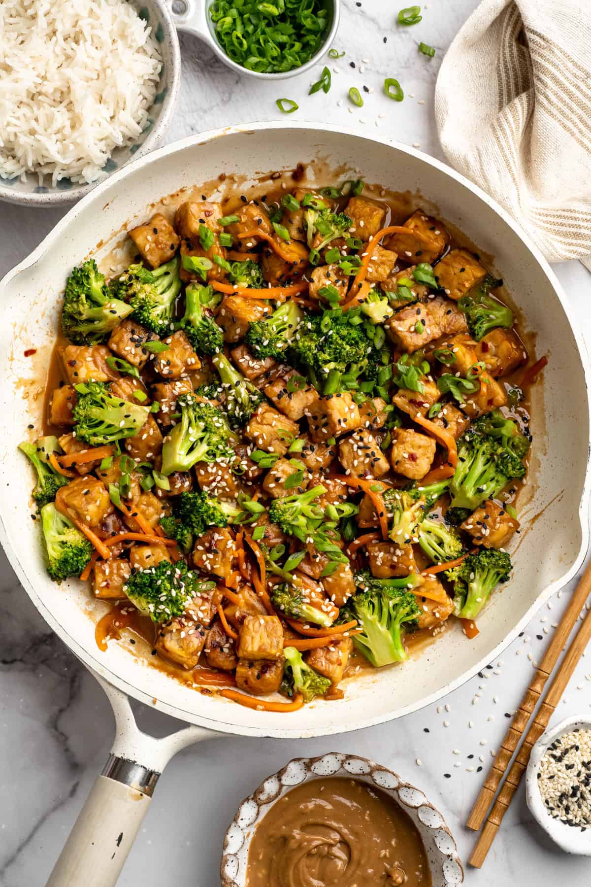 This 35-minute tempeh stir fry combines crispy golden tempeh, tender veggies, and a creamy, savoury-sweet Thai-style peanut sauce. Overhead image of tempeh stir fry with peanut sauce in a pan.