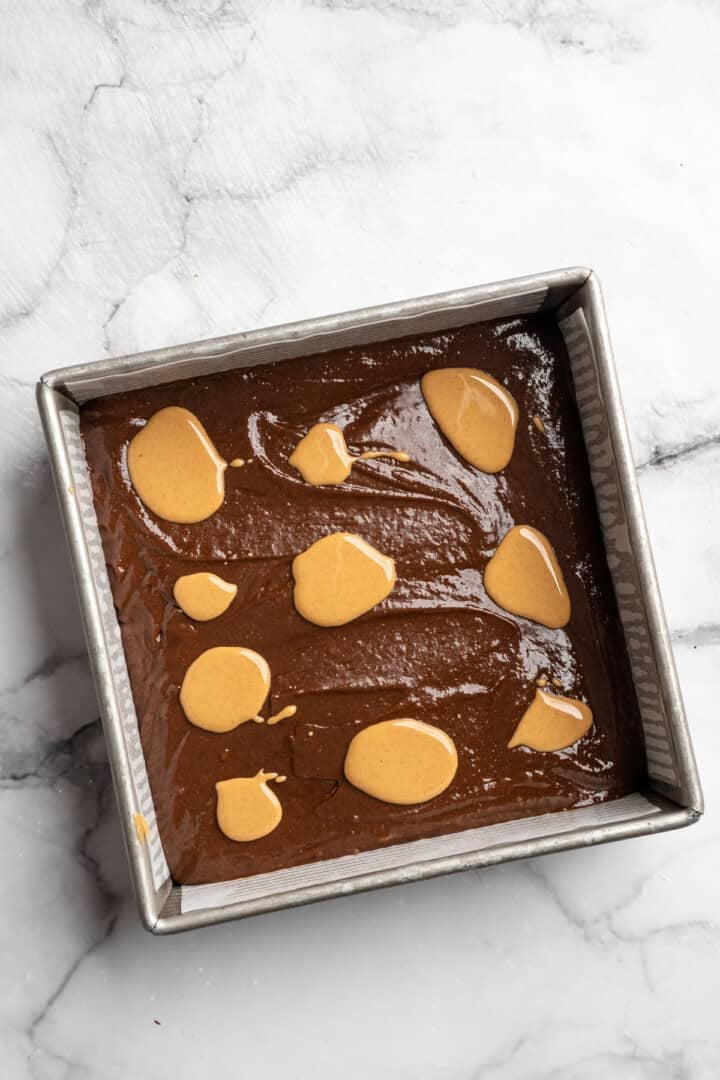 Peanut butter swirl brownies are wonderfully fudge-y, perfectly chewy, and complete with a salty ribbon of peanut butter swirled throughout. Adding dollops of softened peanut butter to a pan full of vegan brownie batter.