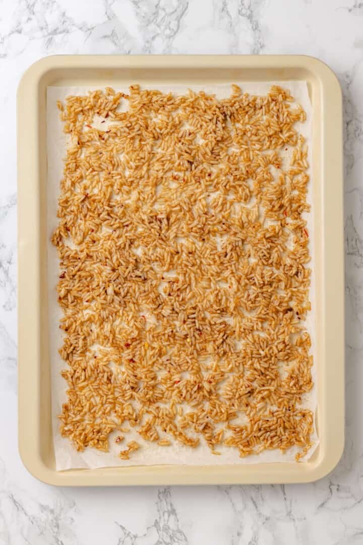 This crispy rice salad is made with soy-infused baked rice tossed with crunchy veggies, caramelized roasted tofu, and Thai peanut sauce. Day-old rice tossed with sesame oil, soy sauce, chili flakes, and garlic powder, spread over a baking sheet.