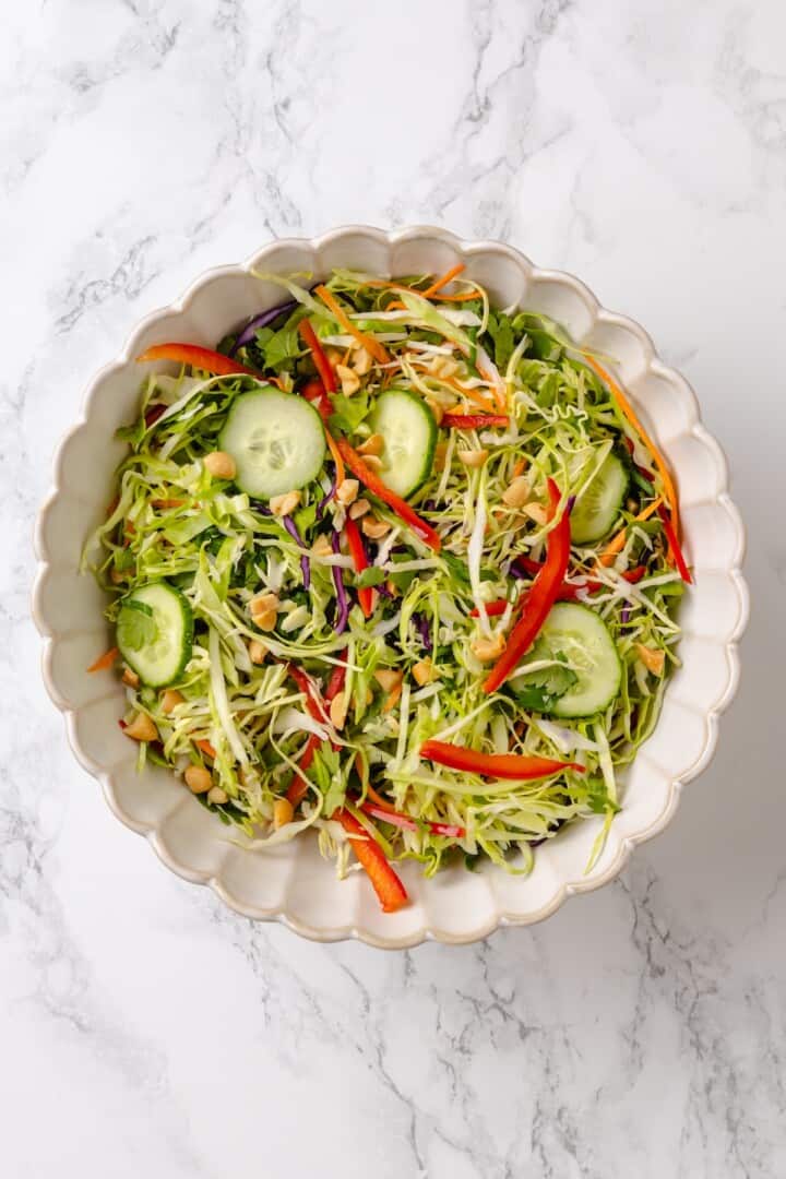 This crispy rice salad is made with soy-infused baked rice tossed with crunchy veggies, caramelized roasted tofu, and Thai peanut sauce. Coleslaw mix, veggies, herbs, and peanuts tossed together in a salad bowl.