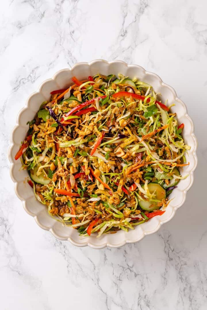 This crispy rice salad is made with soy-infused baked rice tossed with crunchy veggies, caramelized roasted tofu, and Thai peanut sauce. Tossing together crispy rice, baked tofu, crunchy veggies, and peanut sauce to a salad bowl.