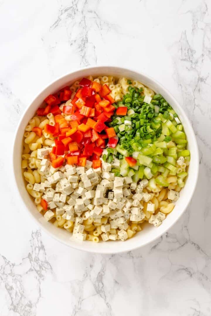 Creamy and crunchy, this macaroni salad recipe is made with crumbled tofu and a touch of kala namak for that old-school eggy flavor. Cooked elbow mac, seasoned tofu, bell pepper, celery, and green onion in a mixing bowl.