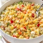 A spoon lifting some vegan mac salad from a serving bowl.