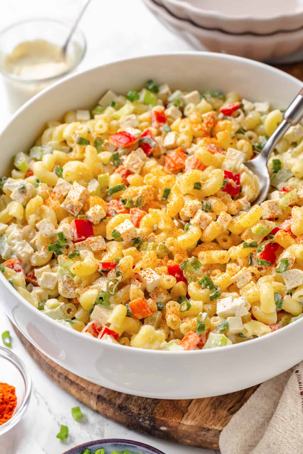 Creamy and crunchy, this macaroni salad recipe is made with crumbled tofu and a touch of kala namak for that old-school eggy flavor. A spoon lifting some vegan mac salad from a serving bowl.