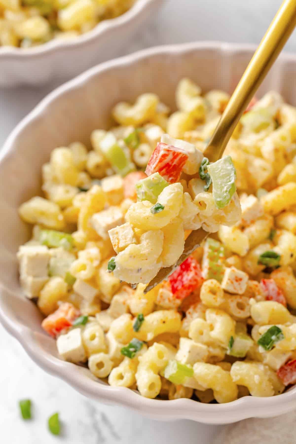 Creamy and crunchy, this macaroni salad recipe is made with crumbled tofu and a touch of kala namak for that old-school eggy flavor. A fork lifting a bite of vegan mac salad from a bowl.