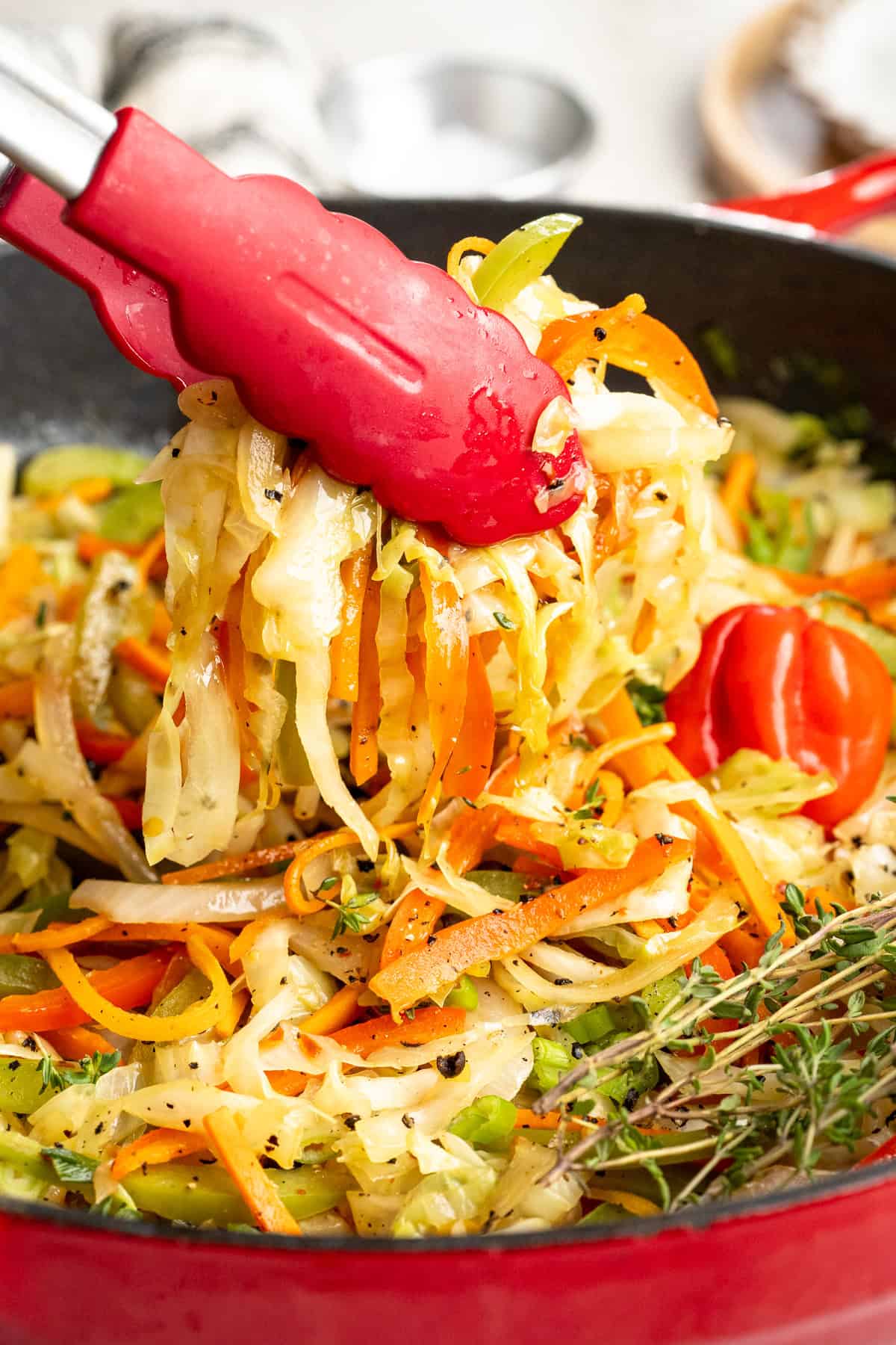This Jamaican steamed cabbage recipe uses simple cooking methods and simple ingredients to infuse veggies with sweet, savoury island flavour. Tongs lifting Jamaican steamed cabbage from a Dutch oven.