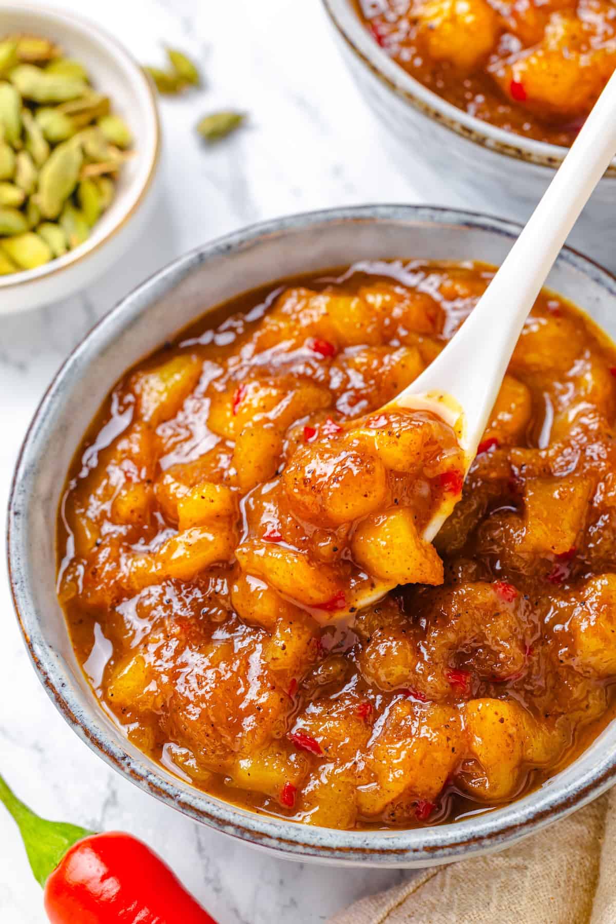 Sweet, savoury, and just a little spicy, this smooth, chunky mango chutney marries traditional Jamaican and Indian flavours beautifully. A spoon tipping into a bowl of mango chutney.