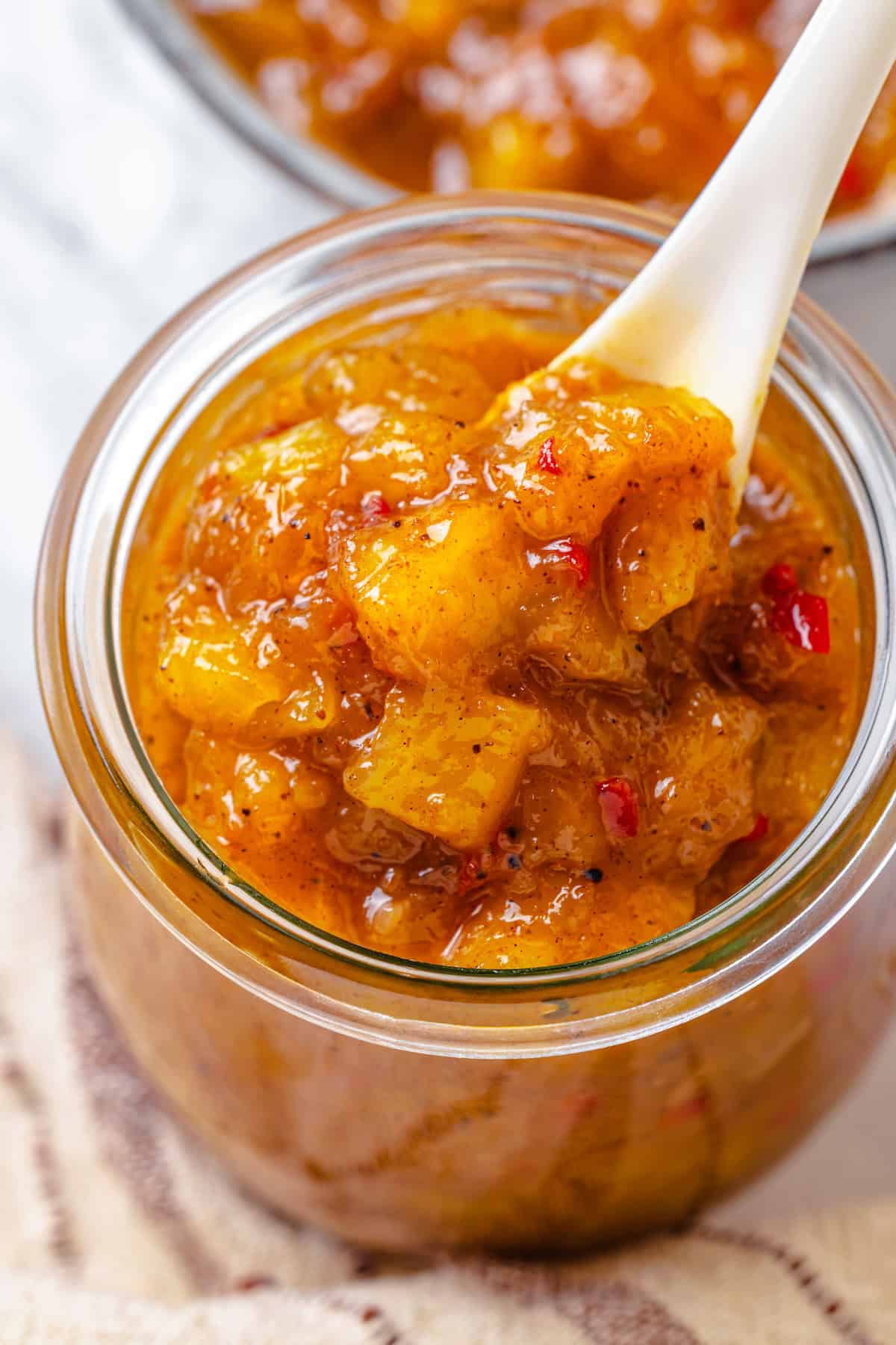 Sweet, savoury, and just a little spicy, this smooth, chunky mango chutney marries traditional Jamaican and Indian flavours beautifully. A spoon dipping into a jar of mango chutney.