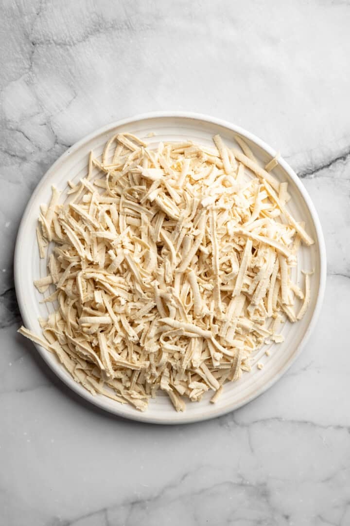 This shredded tofu is tossed in a savoury sauce and baked to crispy golden brown. It's the perfect protein addition to any vegan meal. Shredded tofu on a plate.