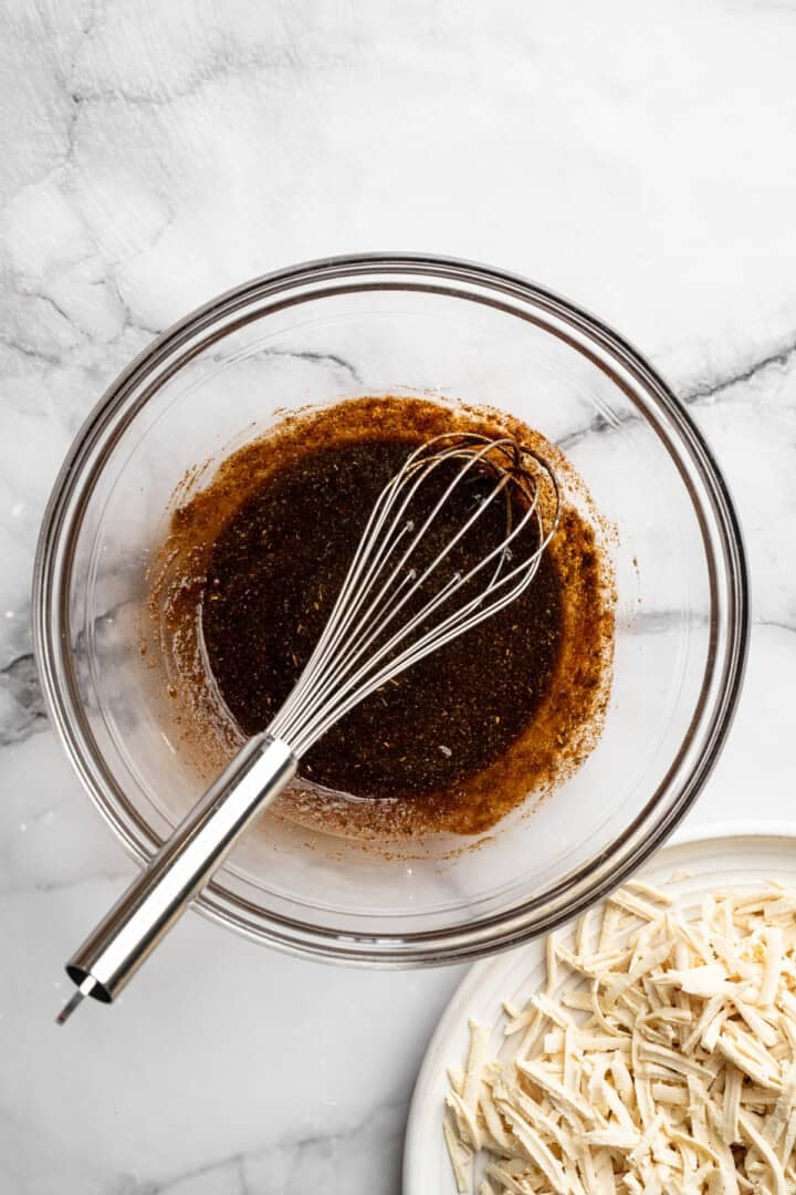 This shredded tofu is tossed in a savoury sauce and baked to crispy golden brown. It's the perfect protein addition to any vegan meal. Whisking together oil, soy sauce, maple syrup, and seasonings to marinate shredded tofu.