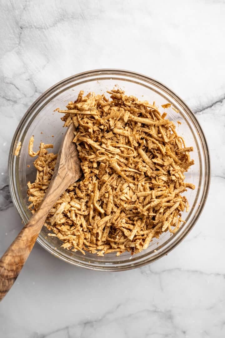 This shredded tofu is tossed in a savoury sauce and baked to crispy golden brown. It's the perfect protein addition to any vegan meal. Tossing shredded tofu in a soy sauce marinade.