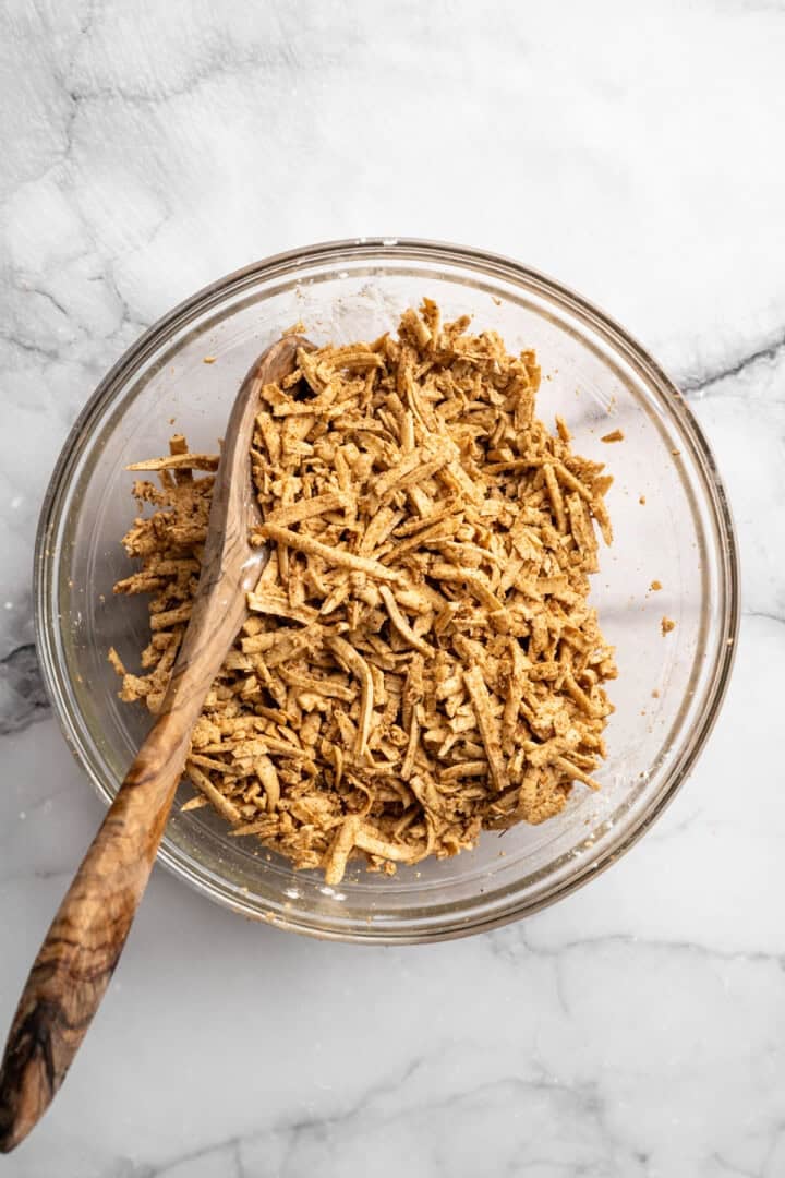 This shredded tofu is tossed in a savoury sauce and baked to crispy golden brown. It's the perfect protein addition to any vegan meal. Tossing saucy shredded tofu with cornstarch.