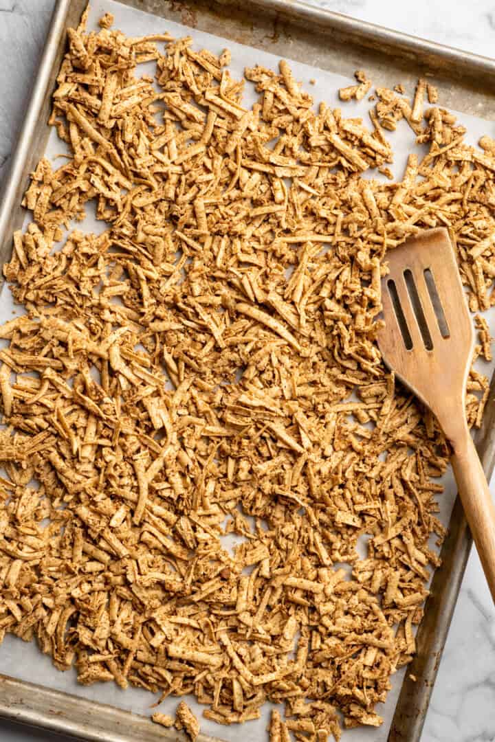 This shredded tofu is tossed in a savoury sauce and baked to crispy golden brown. It's the perfect protein addition to any vegan meal. Marinated shredded tofu spread over a sheet pan.