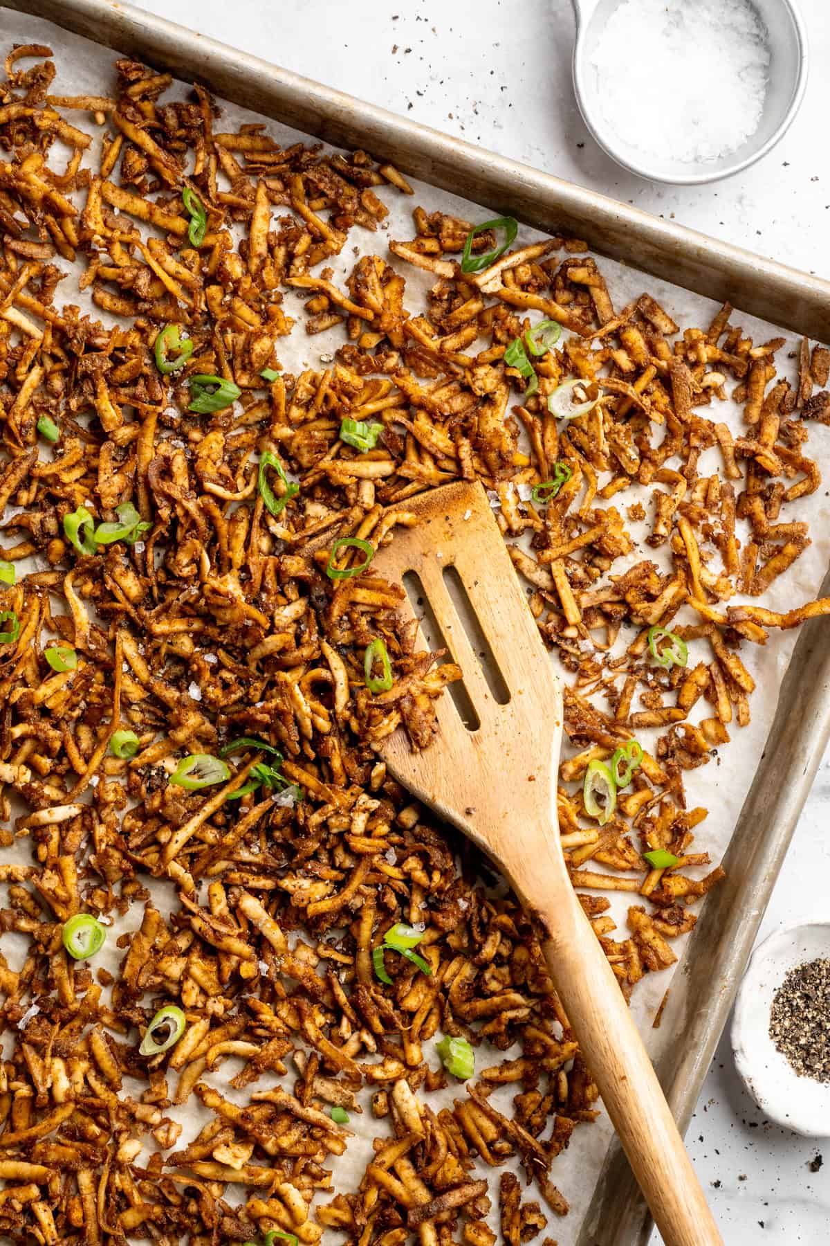 This shredded tofu is tossed in a savoury sauce and baked to crispy golden brown. It's the perfect protein addition to any vegan meal. Shredded tofu on a sheet pan with sliced green onions.