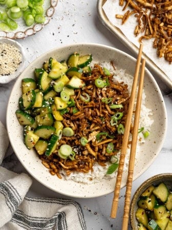A bowl of shredded tofu served over rice with Asian cucumber salad.