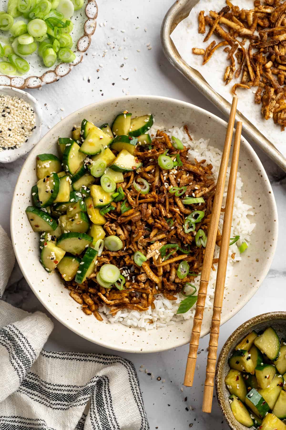This shredded tofu is tossed in a savoury sauce and baked to crispy golden brown. It's the perfect protein addition to any vegan meal. A bowl of shredded tofu served over rice with Asian cucumber salad.