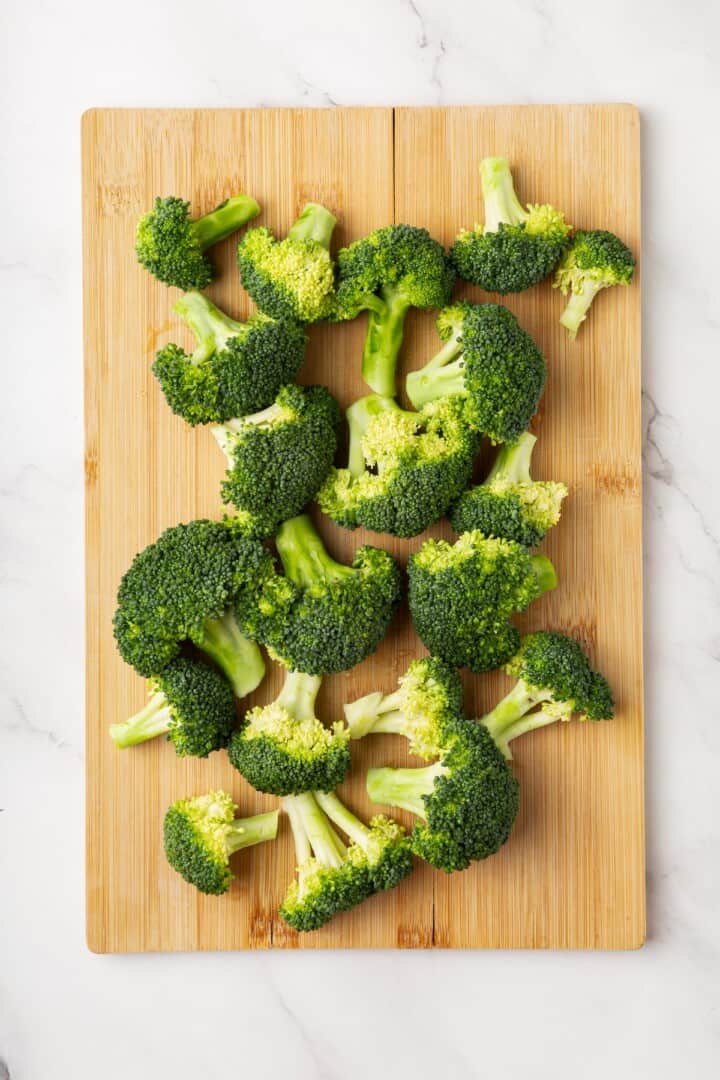 Cheesy vegan smashed broccoli is the perfect way to mix up your veggie routine. Served with a creamy garlic sauce, it's sure to impress. Broccoli florets in a cutting board.