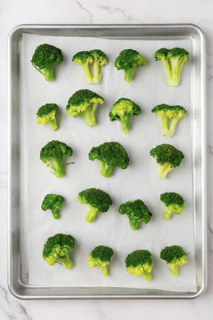 Cheesy vegan smashed broccoli is the perfect way to mix up your veggie routine. Served with a creamy garlic sauce, it's sure to impress. Broccoli florets arranged on a baking sheet.