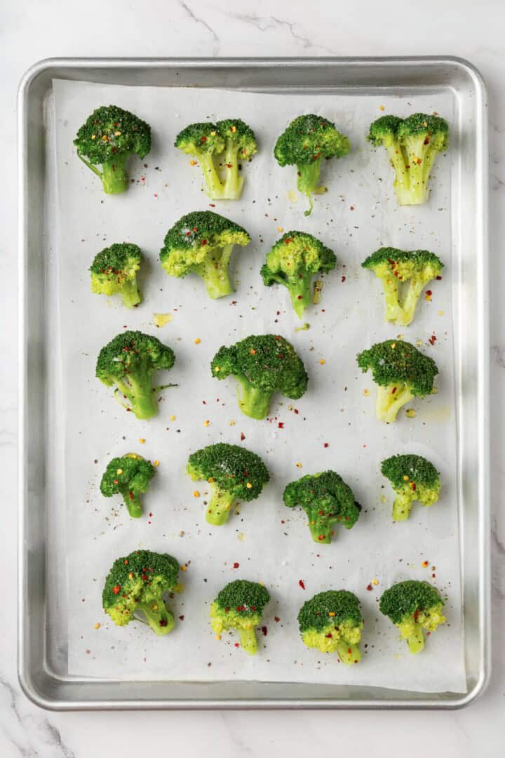 Cheesy vegan smashed broccoli is the perfect way to mix up your veggie routine. Served with a creamy garlic sauce, it's sure to impress. Seasoned broccoli florets arranged on a baking sheet.