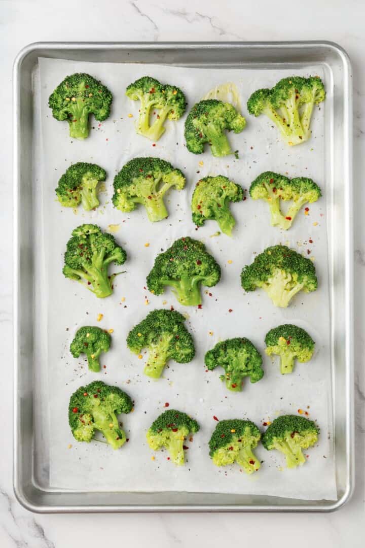 Cheesy vegan smashed broccoli is the perfect way to mix up your veggie routine. Served with a creamy garlic sauce, it's sure to impress. Smashed, seasoned broccoli florets arranged on a baking sheet.