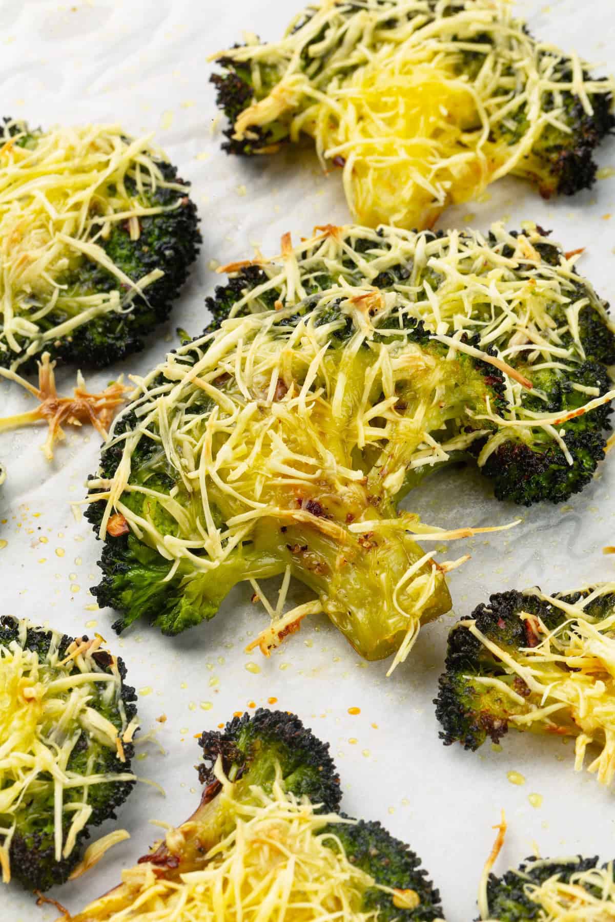 Cheesy vegan smashed broccoli is the perfect way to mix up your veggie routine. Served with a creamy garlic sauce, it's sure to impress. Close-up image of cheesy smashed broccoli on a sheet pan.