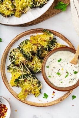 A plate of smashed broccoli with a bowl of vegan creamy garlic sauce.