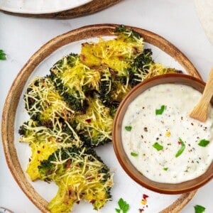 A plate of smashed broccoli with a bowl of vegan creamy garlic sauce.