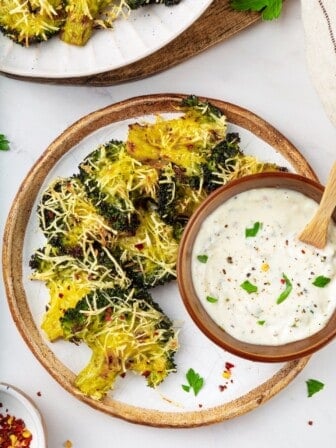 A plate of smashed broccoli with a bowl of vegan creamy garlic sauce.