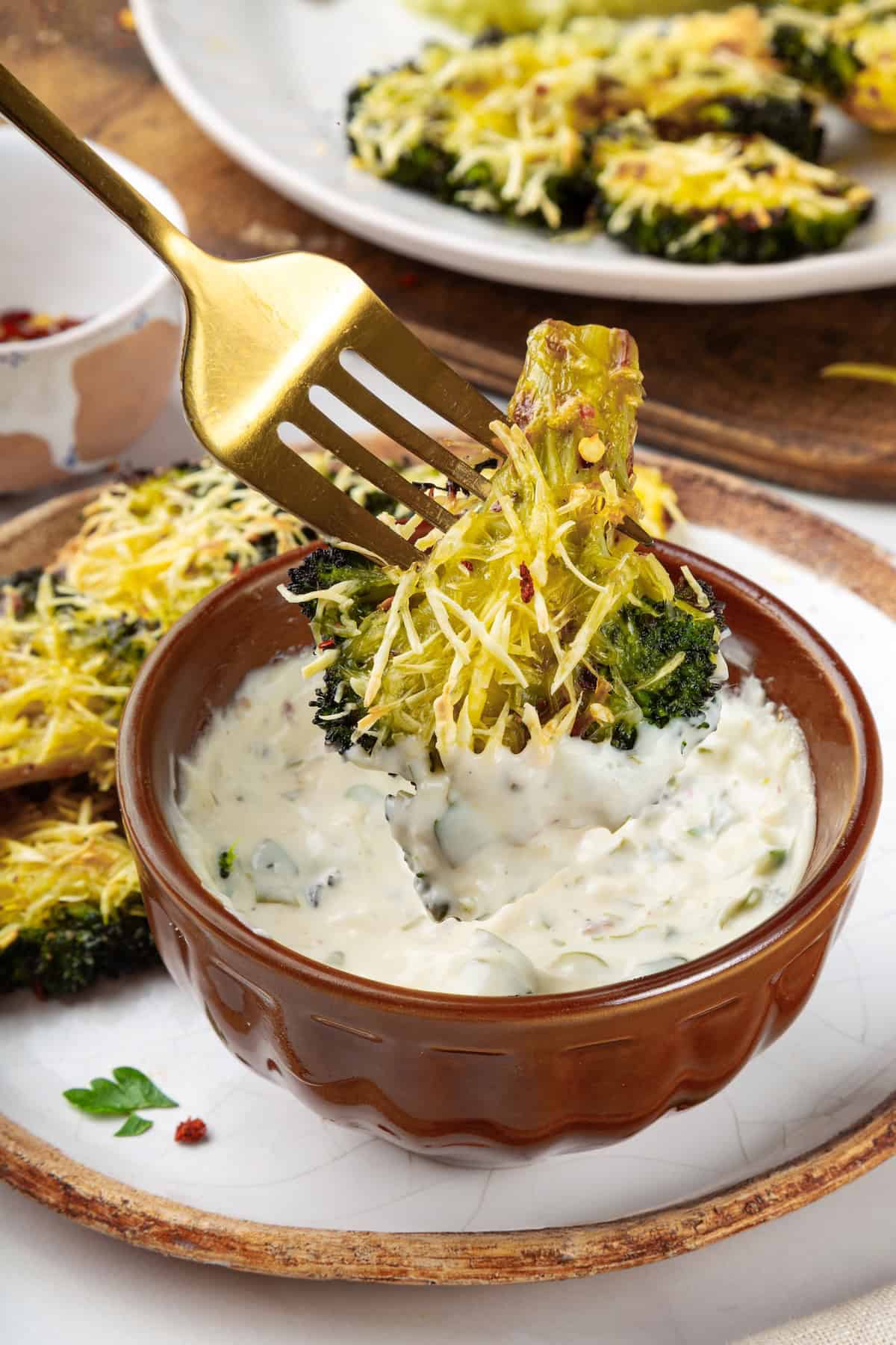 Cheesy vegan smashed broccoli is the perfect way to mix up your veggie routine. Served with a creamy garlic sauce, it's sure to impress. Dipping smashed broccoli into creamy garlic sauce.