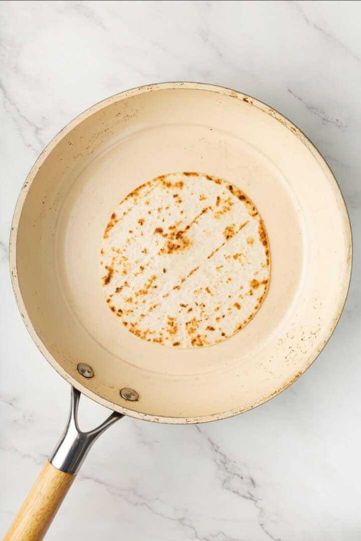 These vegan soy curl tacos pair perfectly crispy soy curl "chicken" with classic taco toppings and the BEST tangy, creamy lime sauce. Warming a tortilla in a pan.