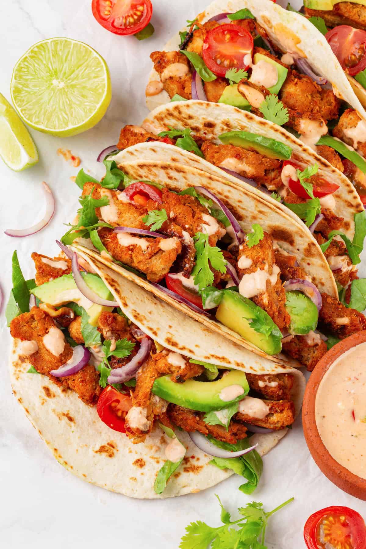 These vegan soy curl tacos pair perfectly crispy soy curl "chicken" with classic taco toppings and the BEST tangy, creamy lime sauce. Overhead image of soy curl tacos on a work surface.