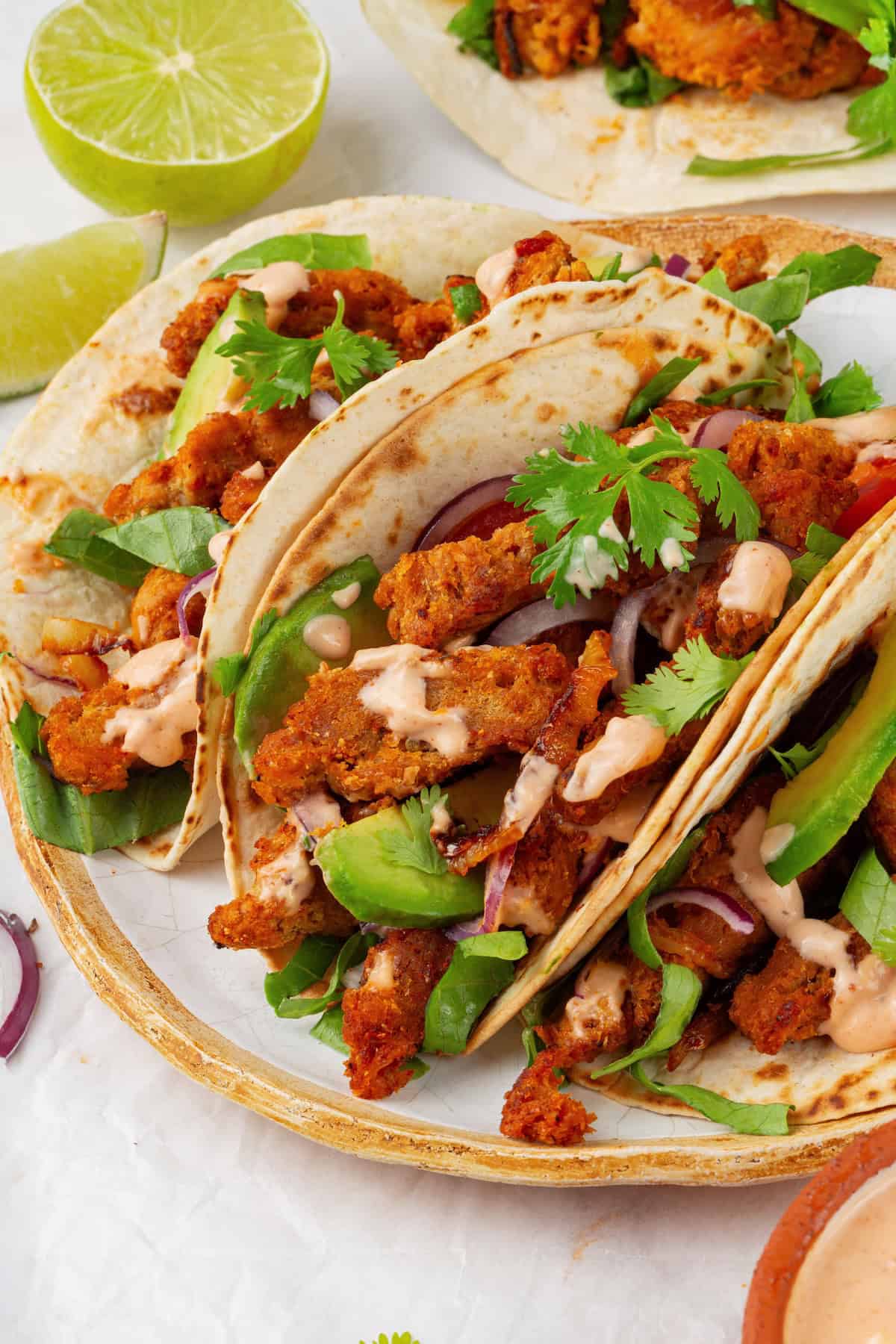 These vegan soy curl tacos pair perfectly crispy soy curl "chicken" with classic taco toppings and the BEST tangy, creamy lime sauce. Close-up of three soy curl tacos on a plate.