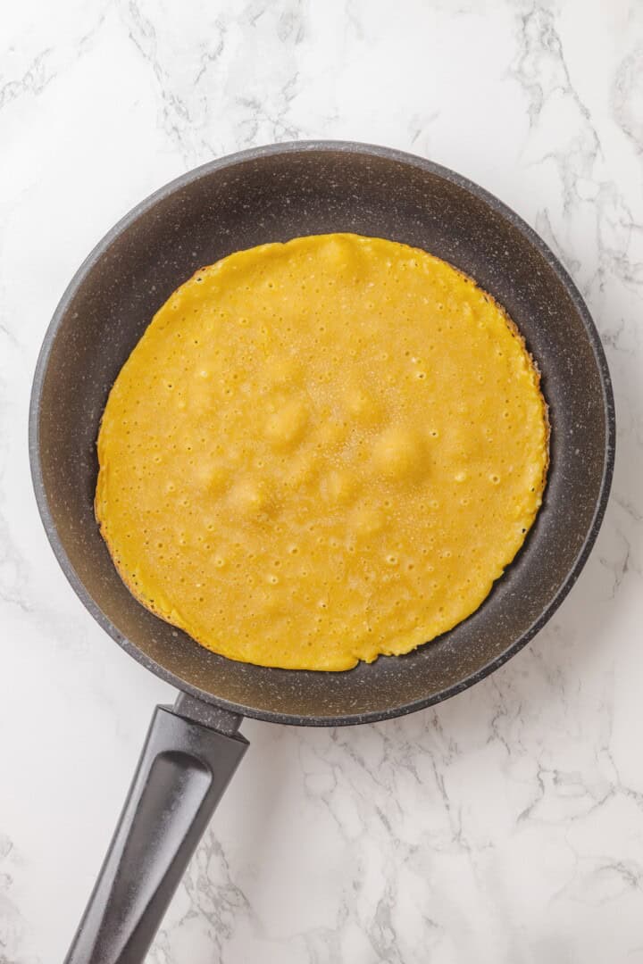 Start today right with this vegan omelette! Chickpea flour and water combine to make a tender omelette filled with veggies and vegan cheese. Cooking chickpea flour omelette batter in a skillet.