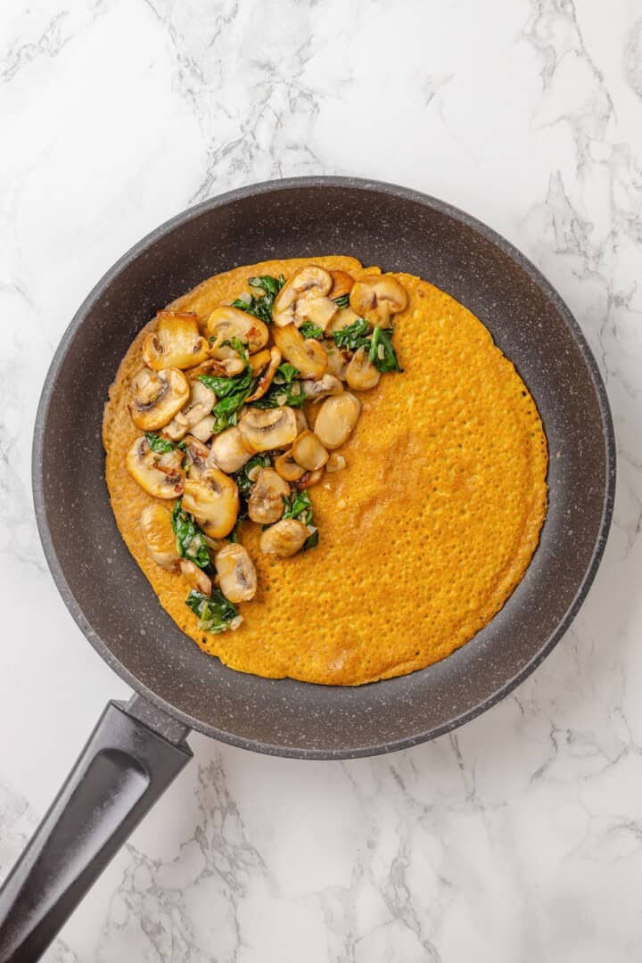 Start today right with this vegan omelette! Chickpea flour and water combine to make a tender omelette filled with veggies and vegan cheese. Filling a chickpea omelette with sautéed veggies.