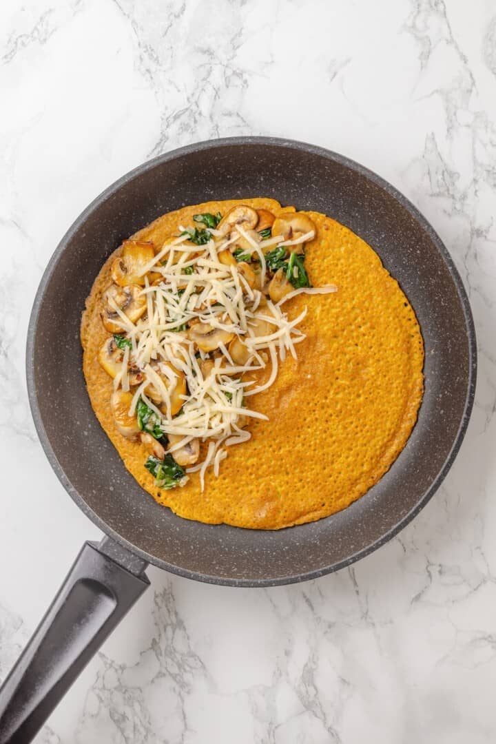 Start today right with this vegan omelette! Chickpea flour and water combine to make a tender omelette filled with veggies and vegan cheese. Adding shredded vegan cheese to a chickpea omelette filled with sautéed veggies.