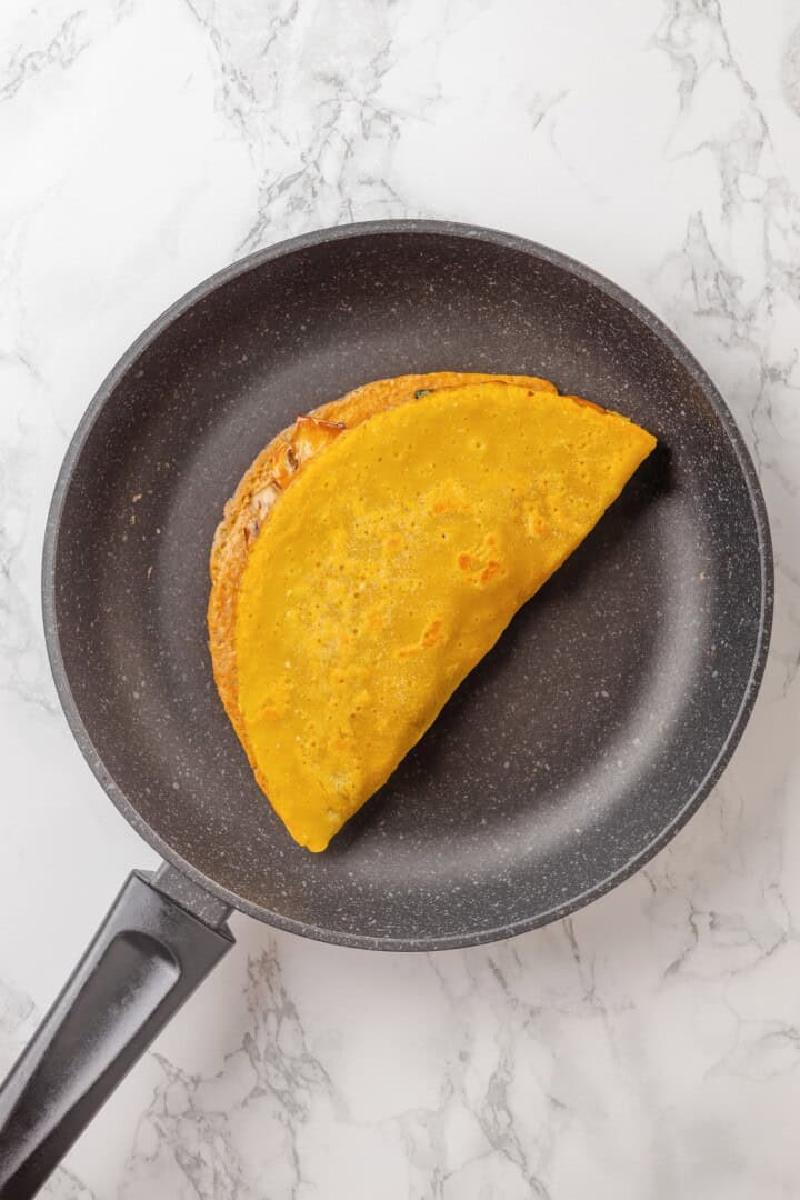 Start today right with this vegan omelette! Chickpea flour and water combine to make a tender omelette filled with veggies and vegan cheese. Folding a chickpea omelette over its filling.