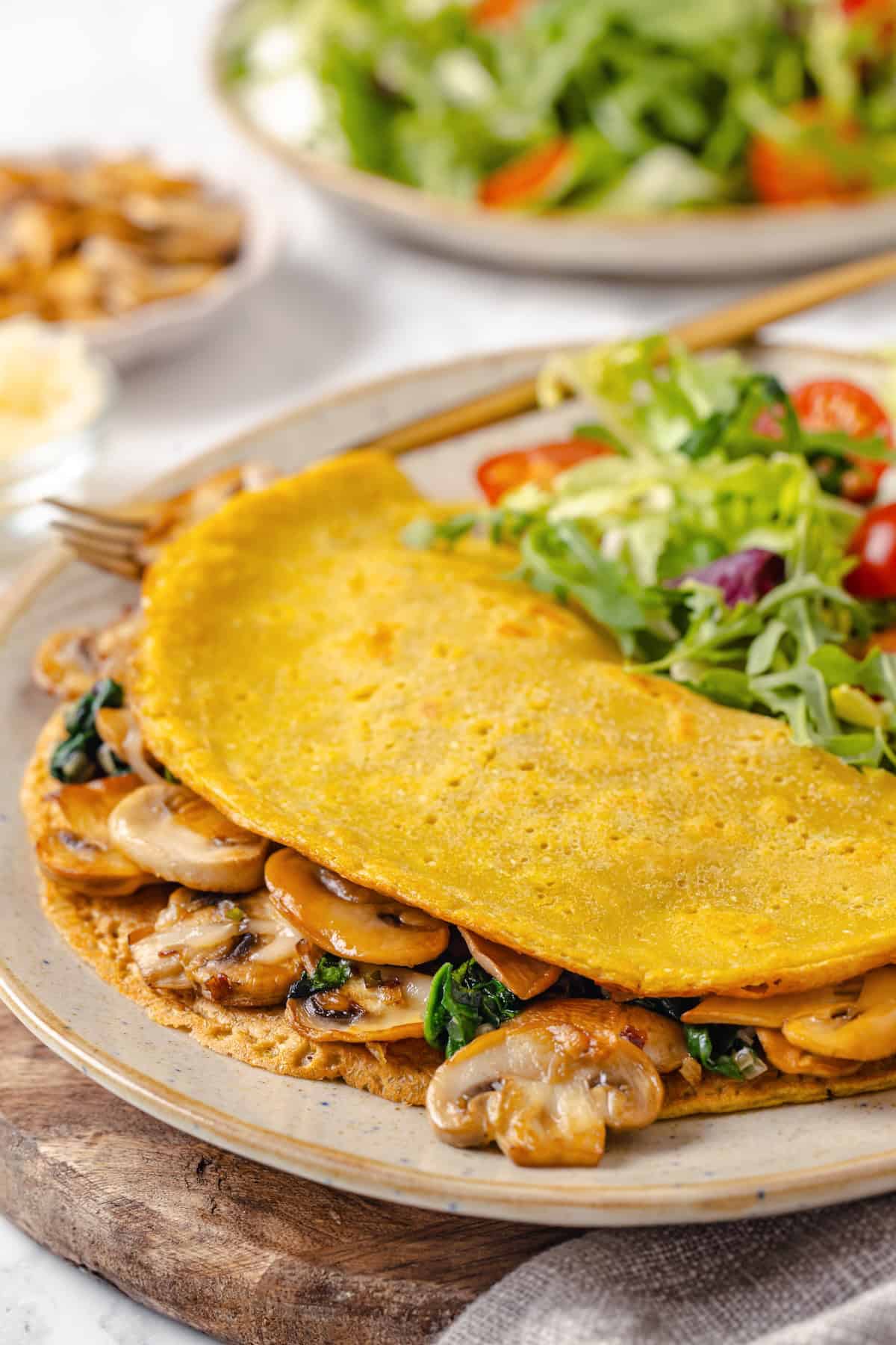 Start today right with this vegan omelette! Chickpea flour and water combine to make a tender omelette filled with veggies and vegan cheese. A vegan chickpea flour omelette on a plate with salad.