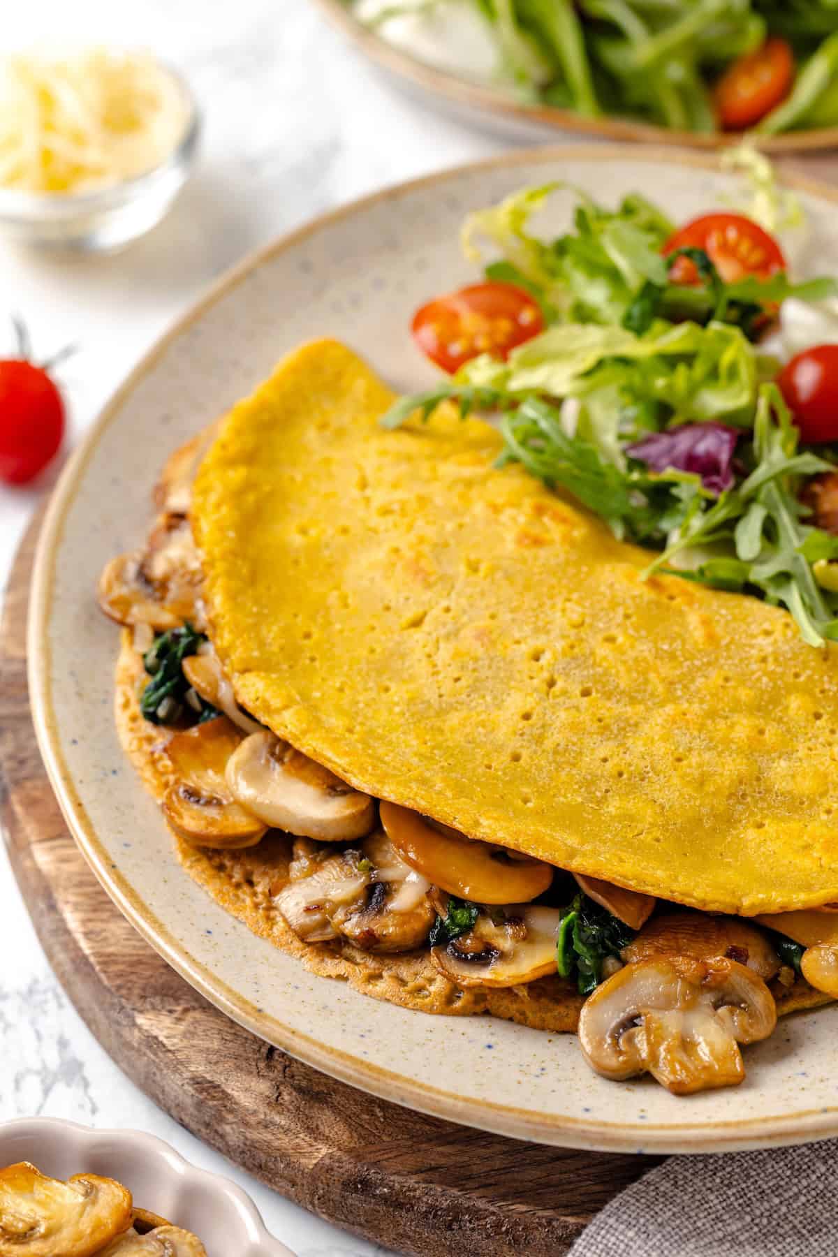 Start today right with this vegan omelette! Chickpea flour and water combine to make a tender omelette filled with veggies and vegan cheese. A vegan chickpea omelette on a plate with salad.